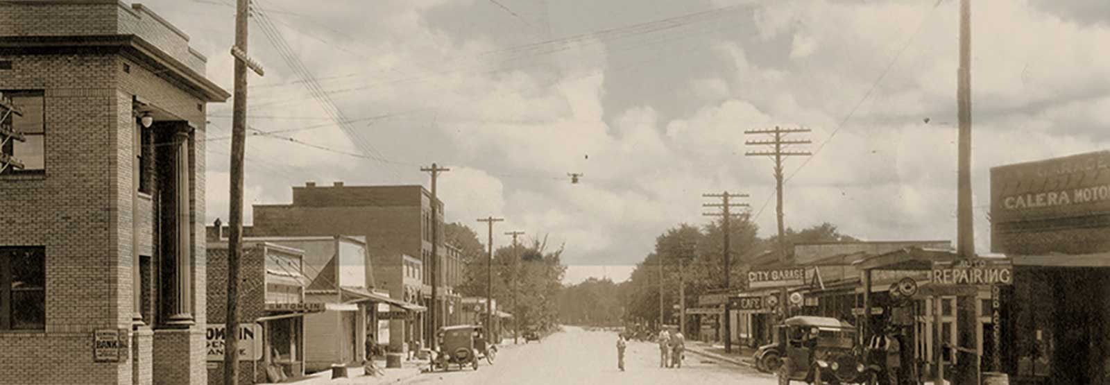 Main street in 1916 showing bank building and other buildings and cars on the street.