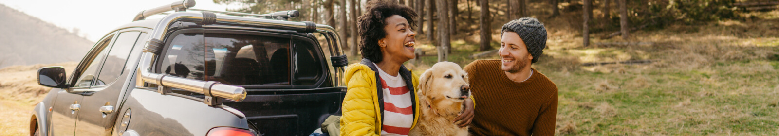 a couple and their dog sitting on a pickup truck bed